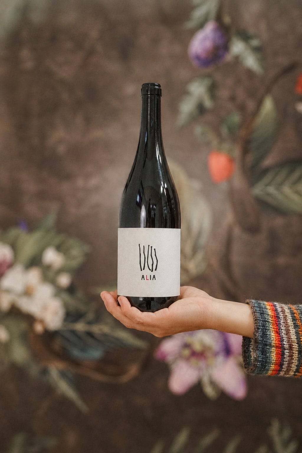 Bottiglia di Alia tenuta in mano davanti a uno sfondo floreale