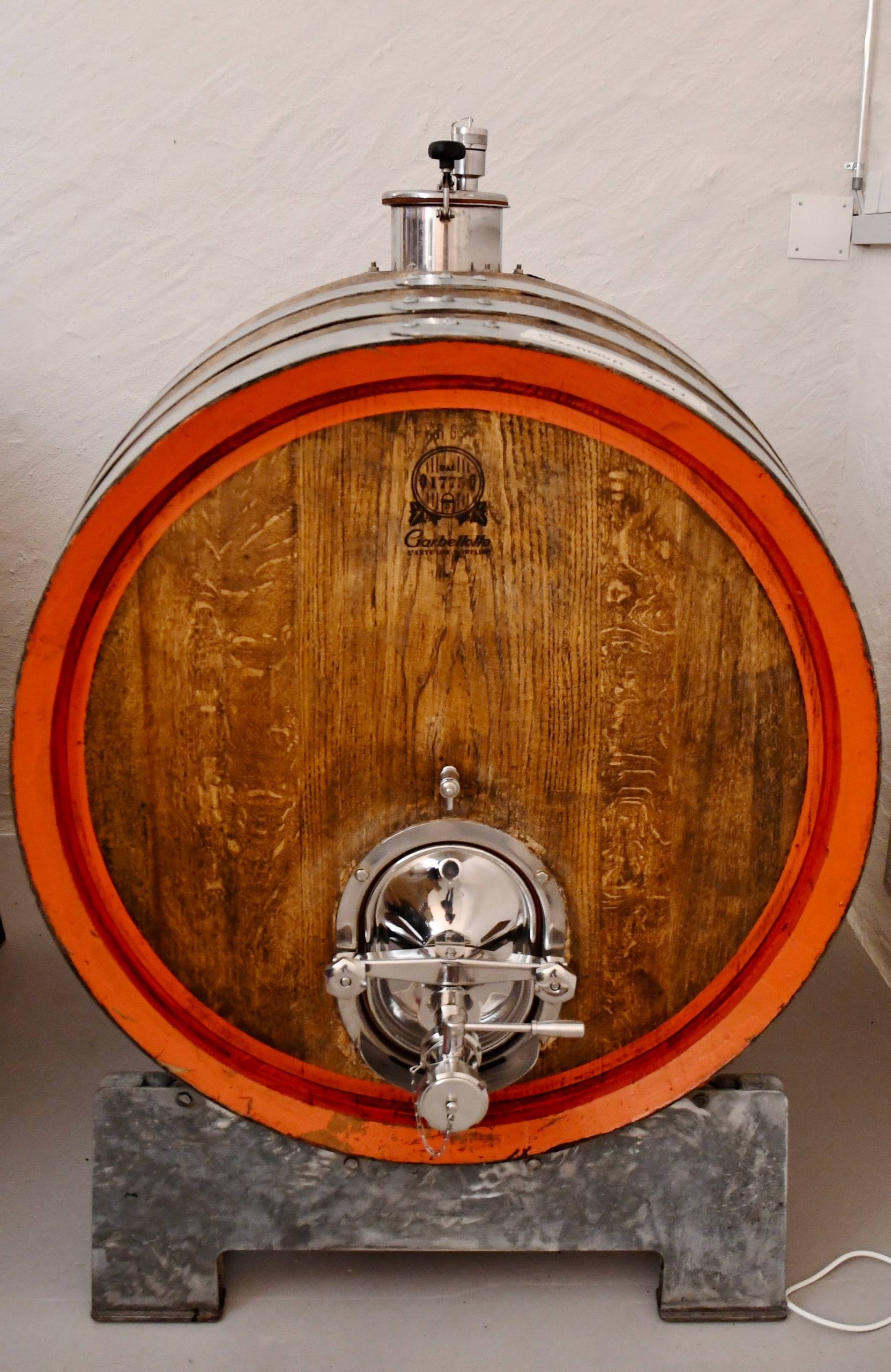 Botte in legno con cerchi arancioni e portella in acciaio nella cantina di Poschiavo